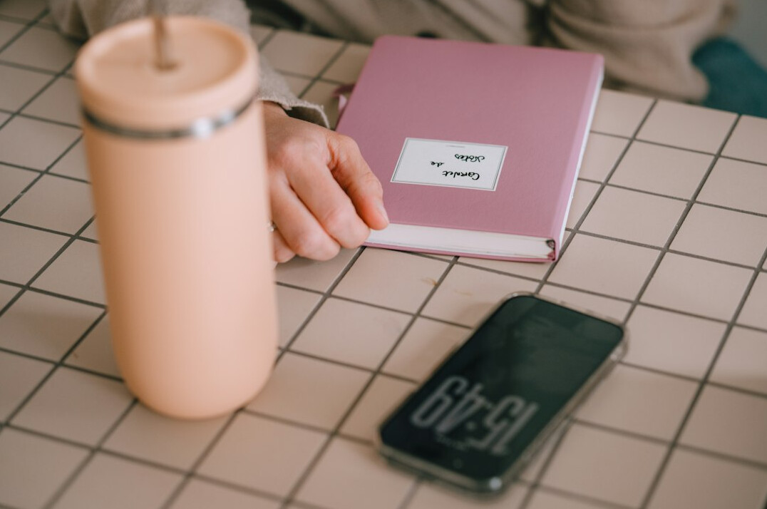 Person writing notes in a notebook next to an open laptop